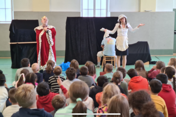 Zwei Schauspieler auf der Bühne, zeigen ein Umwelttheater, Kinder schauen am Boden sitzend zu