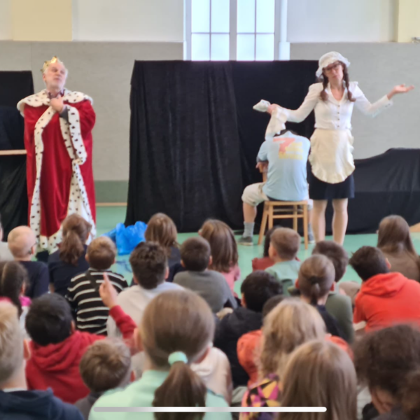 Zwei Schauspieler auf der Bühne, zeigen ein Umwelttheater, Kinder schauen am Boden sitzend zu
