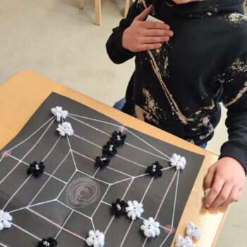 Schüler sitzt am Tisch, vor ihm ein Brettspiel