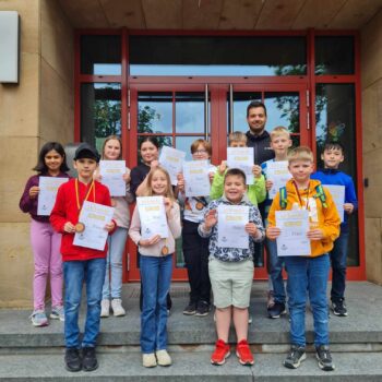 Kinder stehen auf der Treppe und halten ihre Urkunden hoch