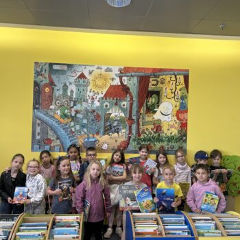 Kinder stehen in der Bibliothek und halten Bücher hoch