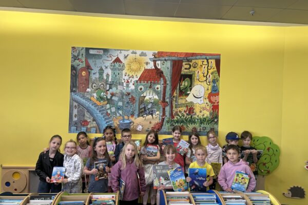 Kinder stehen in der Bibliothek und halten Bücher hoch