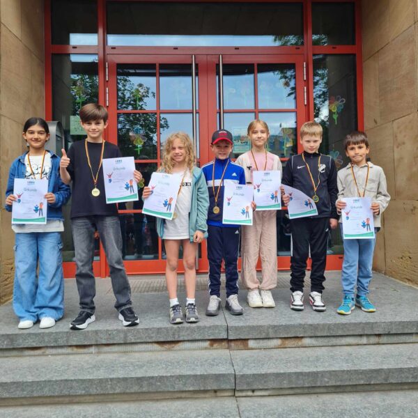 Kinder der 3.Klasse stehen vor dem Schuleingang und halten die Urkunden hoch