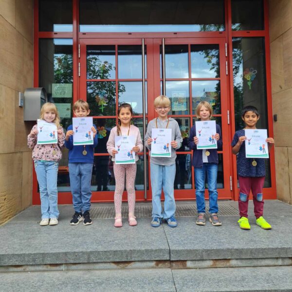 Kinder der der 2.Klasse stehen vor dem Eingang und halten die Urkunden hoch