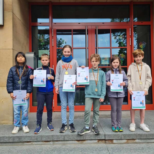 Kinder der 3.Klassen stehen vor dem Schuleingang und halten die Urkunden hoch