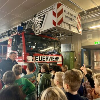 Kinder stehen in der Feuerwache vor einem Feuerwehrfahrzeug