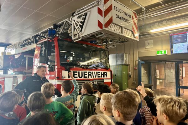 Kinder stehen in der Feuerwache vor einem Feuerwehrfahrzeug