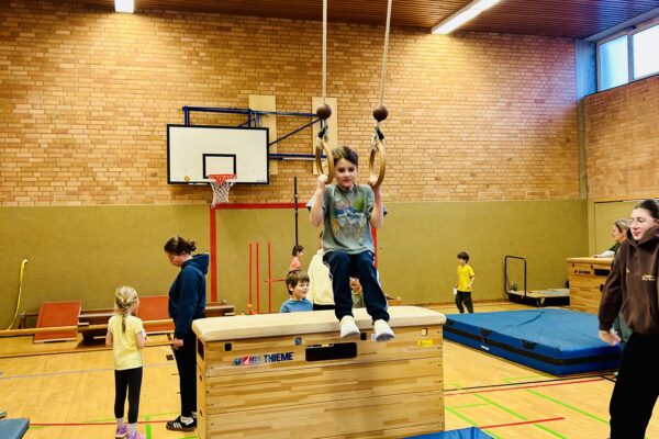 Kind sitzt in den Ringen am Seil in einer Turnhalle