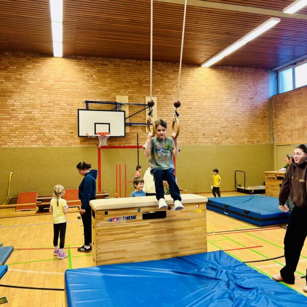 Kind sitzt in den Ringen am Seil in einer Turnhalle